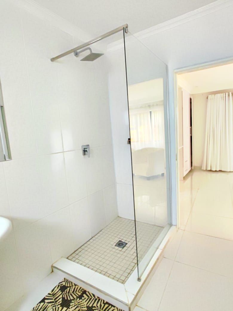 A modern bathroom with a glass shower enclosure, white tiled walls, and a patterned rug.