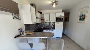 A compact kitchen with white cabinets, a microwave, and a small dining area with two chairs. - Naturiste Cap d'Agde Port Nature 804 (Agde)