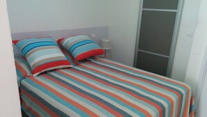 A small, neatly made bed with striped bedding in a room with white walls and a sliding door. - Naturiste Cap d'Agde Port Nature 804 (Agde)
