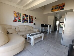 A living room with a beige sofa, a white coffee table, and three colorful paintings on the wall. - Naturiste Cap d'Agde Villa Héliovillage 3 (Agde)