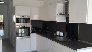A modern kitchen with white cabinets, stainless steel appliances, and a black countertop. - Naturiste Cap d'Agde Villa Héliovillage 3 (Agde)