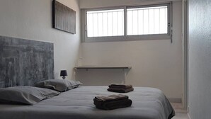 A bedroom with a bed, pillows, a bedside table, a lamp, a window, and a headboard. - Naturiste Cap d'Agde Villa Héliovillage 3 (Agde)