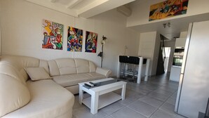 A living room with a beige sofa, a white coffee table, and colorful abstract paintings on the wall. - Naturiste Cap d'Agde Villa Héliovillage 3 (Agde)