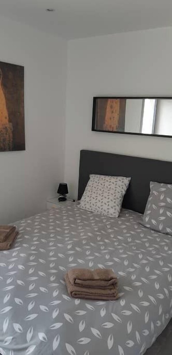 A neatly made bed with a leaf-patterned bedspread, a dark headboard, and a small bedside table with a lamp.