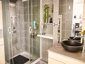 A modern bathroom with a glass-enclosed shower, a vanity with a bowl sink, and a small shelf with toiletries.