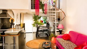 A modern kitchen with a gas stove, a dining area with a table and chairs, a pink sofa with a leopard print throw, and a staircase with a metal railing.
