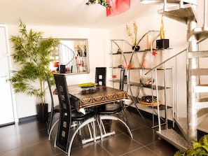 Een eetgedeelte met een tafel, stoelen, een potplant, een spiegel en een trap.