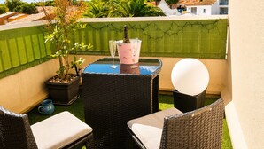 A balcony with wicker furniture, a glass table, a pink bucket with a bottle and glass, and a white spherical object.