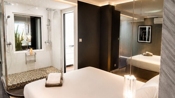 Una habitación de hotel moderna con una cama grande, cabina de ducha de vidrio, baño con espejo y televisor.