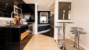 Una cocina moderna con gabinetes negros, electrodomésticos de acero inoxidable y una isla central. Hay dos taburetes con asientos a rayas de cebra.