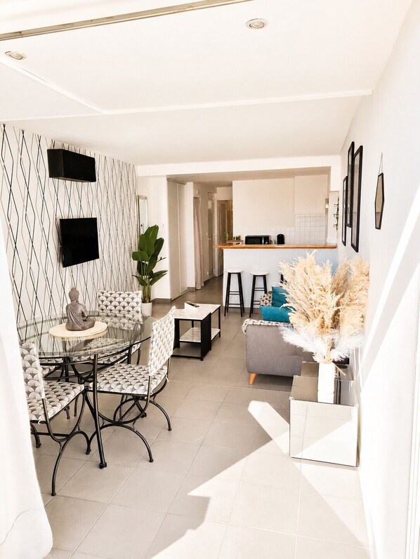 A modern living space with a dining area, kitchen, and a seating area with a sofa and decorative plants.