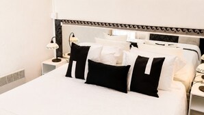 A hotel room with a large bed, a bedside table with a lamp, and a window with sheer curtains.