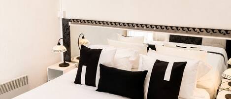 Une chambre d’hôtel avec un grand lit, une table de chevet avec une lampe et une fenêtre avec des rideaux légers.