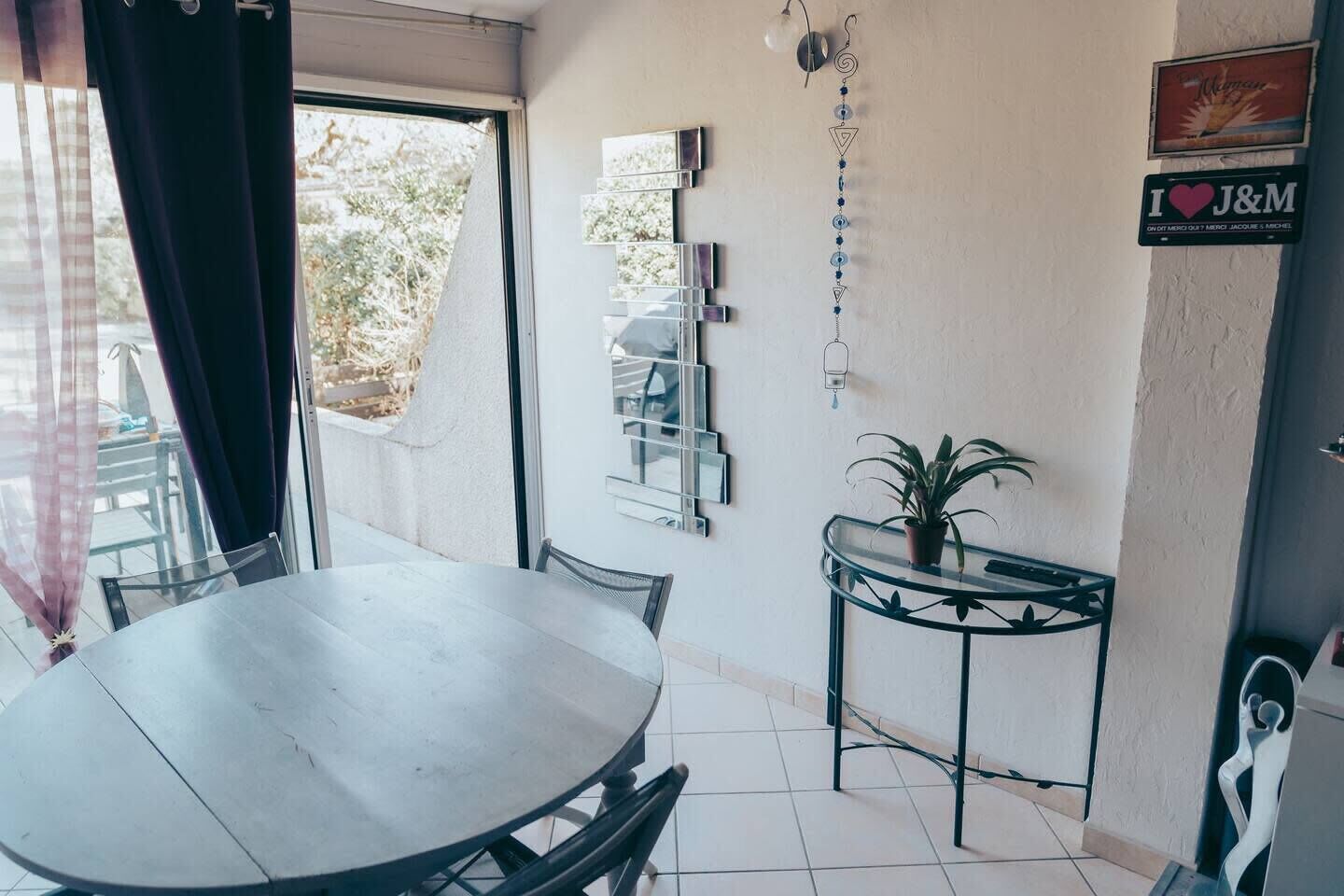 A dining area with a round table and chairs, a small potted plant on a glass table, and a wall-mounted light fixture.