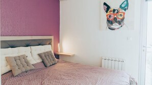Un dormitori amb un llit, un capçal, una obra d'art amb un gat i una finestra.