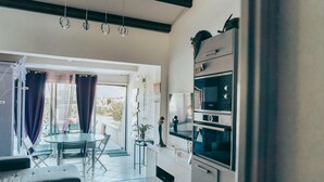 Una cuina moderna amb electrodomèstics integrats, una zona de menjador amb taula i cadires, i un gran finestral amb cortines.