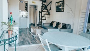 Un saló modern amb una taula de dinar de vidre, un sofà i una escala que condueix a un pis superior.