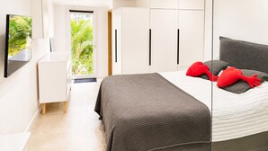 Un dormitorio moderno con cama, armario, televisor y vistas a la vegetación exterior.