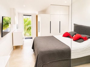 A modern bedroom with a bed, a wardrobe, a television, and a view of greenery outside.