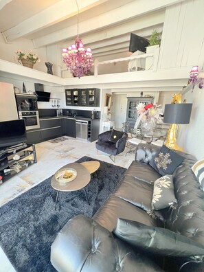 A modern living room with a black leather sofa, a coffee table, and a chandelier.