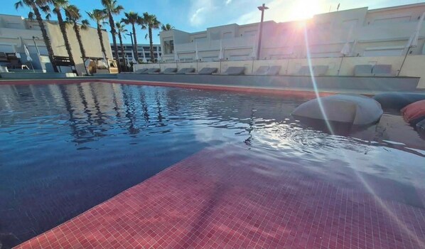 A swimming pool with a tiled edge, palm trees, and a building in the background.