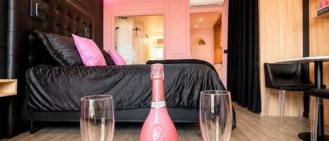 Une chambre d’hôtel moderne avec un lit, une table de chevet sur laquelle se trouve une bouteille de champagne, et deux verres.