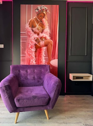Un fauteuil violet dans une piĂšce dont un mur est noir et oĂč lâon trouve un rideau rose.