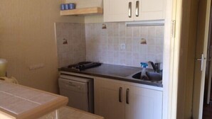 Cocina compacta con armarios blancos, lavavajillas y un lavabo con un pulverizador.