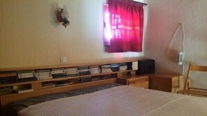Un dormitorio con una cama grande, un cabecero de madera, una mesita de noche con una lámpara y una ventana con cortina roja.