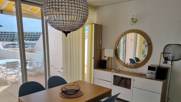 A dining area with a wooden table, blue chairs, a woven basket, a large mirror, and a floor lamp.