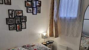 A bedroom with a bed, a bedside table with a lamp, and a wall with framed pictures.