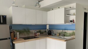 Eine moderne Küche mit weißen Schränken, einer eingebauten Kochinsel mit einer Wandfliesenverkleidung im Strandhausstil und einer Mikrowelle über der Arbeitsfläche.