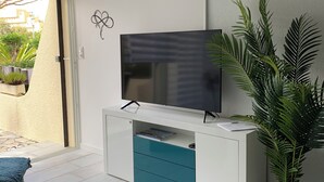 Ein modernes Wohnzimmer mit einem flachbildfernseher an einem weißen Schrank, einem Glastisch und einem Blumentopf.