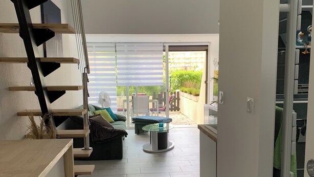 Ein modernes Interieur mit einer Treppe, einem Essbereich mit Tisch und Stühlen und Blick auf einen Garten durch eine Schiebetür.