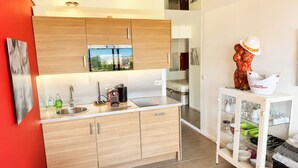 A modern kitchen with wooden cabinets, a built-in oven, a sink, and a dining area with a table and chairs. - Naturiste Cap d'Agde Port Nature 854 (Agde)