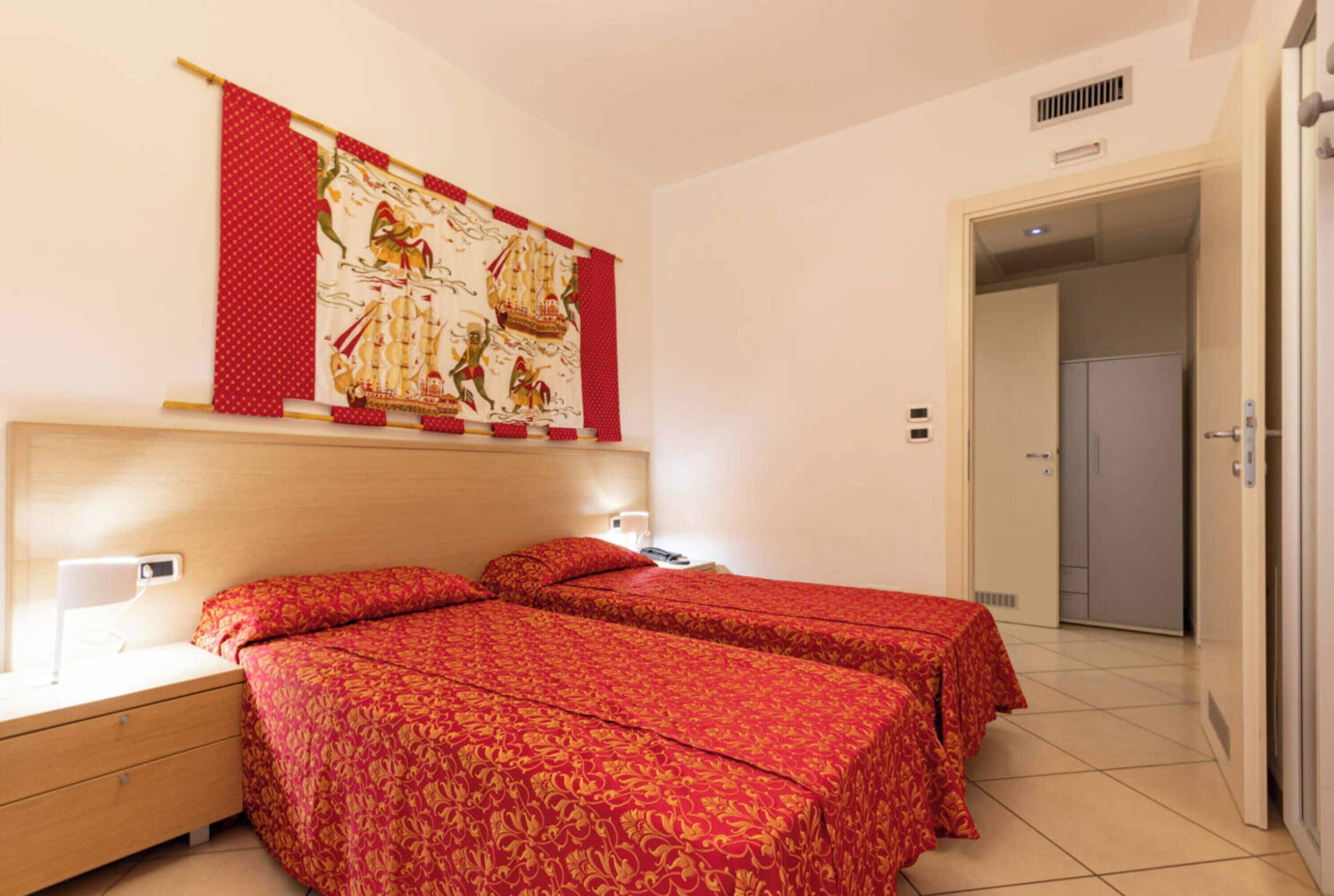 A hotel room with two beds, a nightstand, a wall-mounted lamp, and a door leading to a closet.