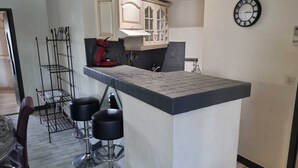 A kitchen with a bar area, two stools, a red appliance, and a clock on the wall. - Naturiste Cap d'Agde Port Nature 544 (Agde)