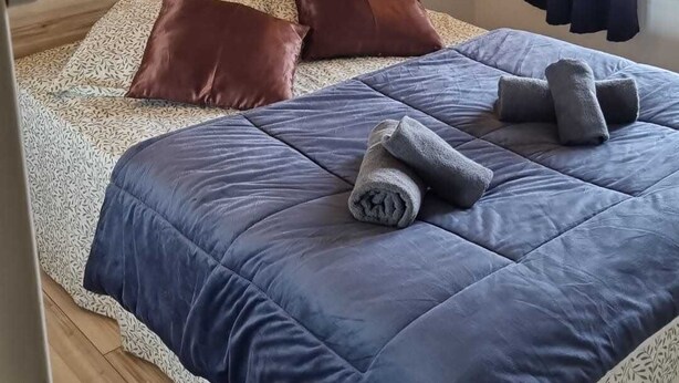 A bedroom with a bed, pillows, a headboard, a wall-mounted light, and a window with curtains. - Naturiste Cap d'Agde Port Nature 544 (Agde)