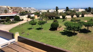 A view of a landscaped garden with neatly trimmed bushes and trees, a clear sky, and a distant view of a coastal area with buildings. - Naturiste Cap d'Agde Port Nature 544 (Agde)