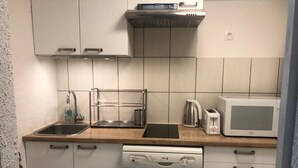 Eine kompakte Küche mit weißen Schränken, einem Geschirrspüler, einer Mikrowelle, einem Wasserkocher und einem Toaster.