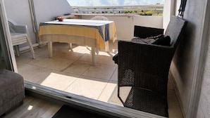 Un balcón con mesa y sillas, un sofá de mimbre y vistas al cielo y las nubes.