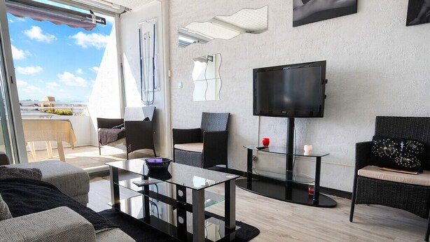 Una sala de estar moderna con un sofá, una mesa de centro de vidrio, un televisor de pantalla plana y un balcón con vistas.