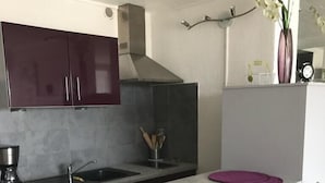 Una cocina compacta con una isla central, taburetes blancos para bar y un salpicadero oscuro.