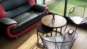 Een moderne woonkamer met een zwart-rode bank, een klein houten tafeltje en twee metalen stoelen.
