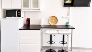A compact kitchen with a microwave, coffee maker, and a TV mounted on the wall.