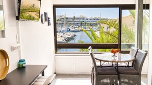 A modern kitchen with a large window, a dining area with wicker chairs, and a TV mounted on the wall.