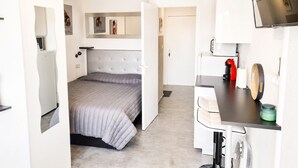 A compact hotel room with a bed, a desk, a chair, a television, and a small kitchenette.