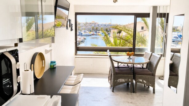 A modern kitchen with a large window, a dining area with wicker chairs, and a view of a marina.