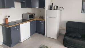 A compact kitchen with dark cabinets, a white refrigerator, a microwave, and a coffee maker on the countertop. - Naturiste Cap d'Agde Héliopolis F 71 (Agde)