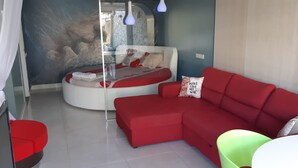 A modern room with a red sofa, a circular bed with a white and red design, and a glass partition.